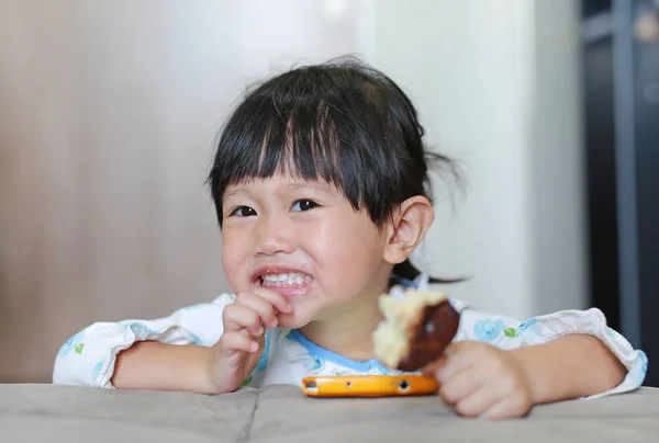Sonriente asiática bebé niña comiendo donut en la habitación. Infancia . — Foto de Stock