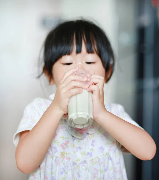 Petite fille mignonne en pyjama boire du lait de verre à l'intérieur le matin . — Photo