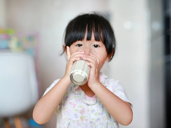 Petite fille mignonne en pyjama boire du lait de verre à l'intérieur le matin . — Photo