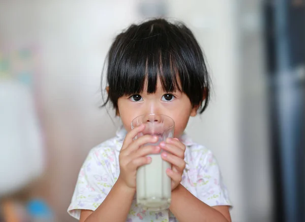 Ładna dziewczynka w piżamy, picie mleka z szkła kryty o poranku. — Zdjęcie stockowe