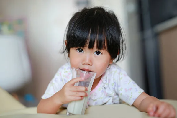 Menina bonito em pijama beber leite de vidro interior na parte da manhã . — Fotografia de Stock
