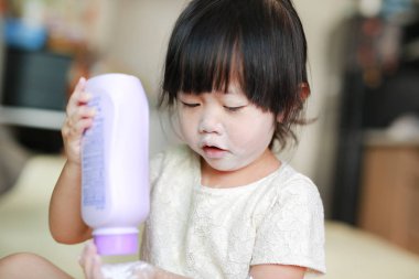 Portrait of cute little girl with baby powder on her face. Little girl pour the talcum to the hand. clipart