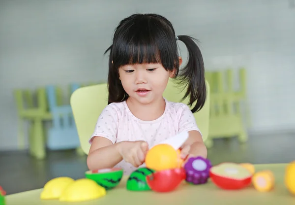 Enfant fille à la table joue des fruits artificiels dans la chambre des enfants . — Photo