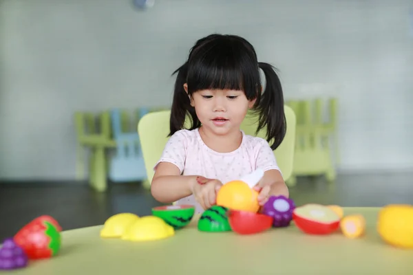 Enfant fille à la table joue des fruits artificiels dans la chambre des enfants . — Photo