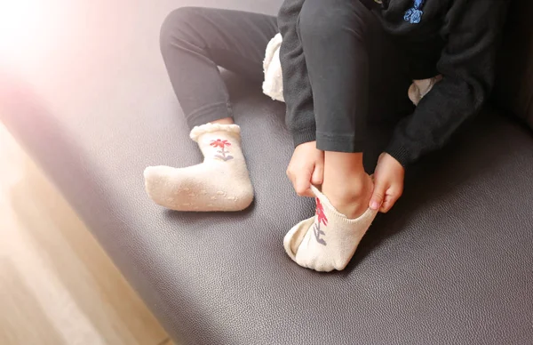 Niña tratando de poner un calcetines en el sofá marrón . —  Fotos de Stock