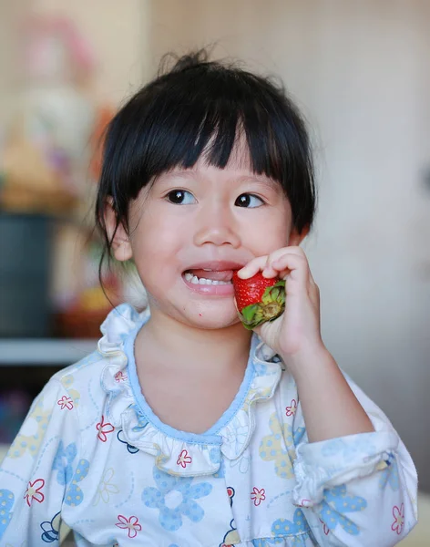 Liten flicka i pyjamas äta jordgubbar hemma. — Stockfoto