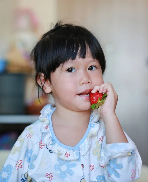 Liten flicka i pyjamas äta jordgubbar hemma. — Stockfoto
