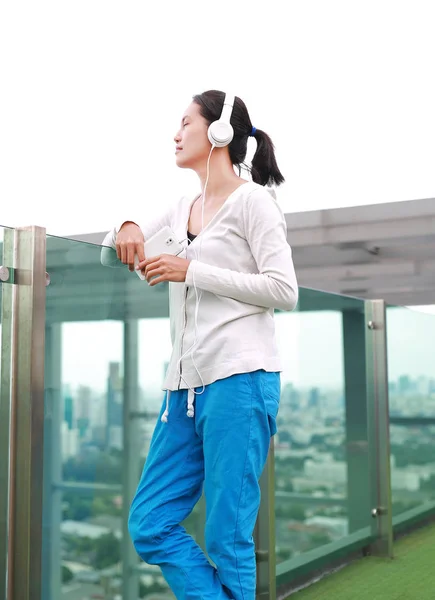 Jovem mulher asiática ouvindo música em fones de ouvido no telhado do edifício. Menina relaxante feliz — Fotografia de Stock
