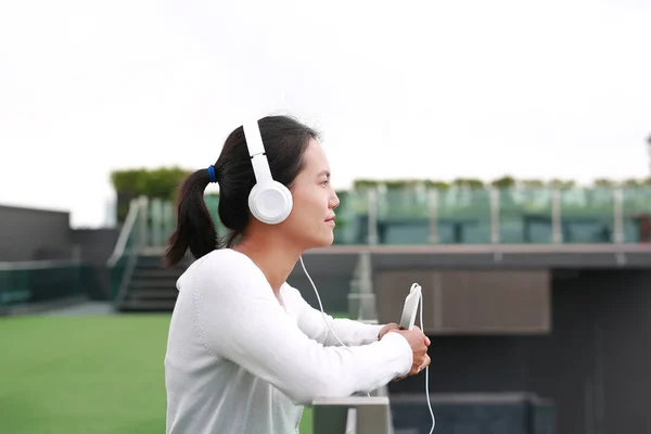 Jeune femme asiatique écoutant de la musique dans les écouteurs sur le toit du bâtiment. Heureuse fille relaxante — Photo