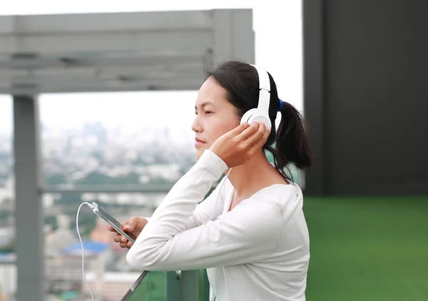 Mujer asiática joven escuchando música en auriculares en la azotea del edificio. Feliz chica relajante — Foto de Stock