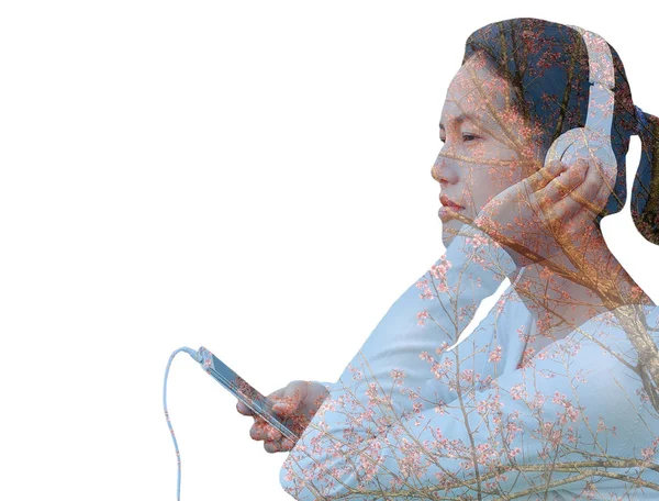 Mujer de doble exposición escuchando música en auriculares con árbol de sakura — Foto de Stock