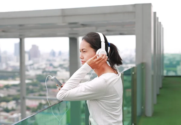 Jeune femme asiatique écoutant de la musique dans les écouteurs sur le toit du bâtiment. Heureuse fille relaxante — Photo
