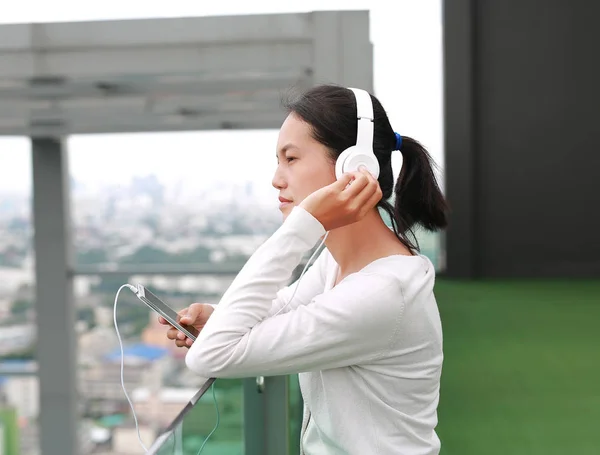 Jeune femme asiatique écoutant de la musique dans les écouteurs sur le toit du bâtiment. Heureuse fille relaxante — Photo