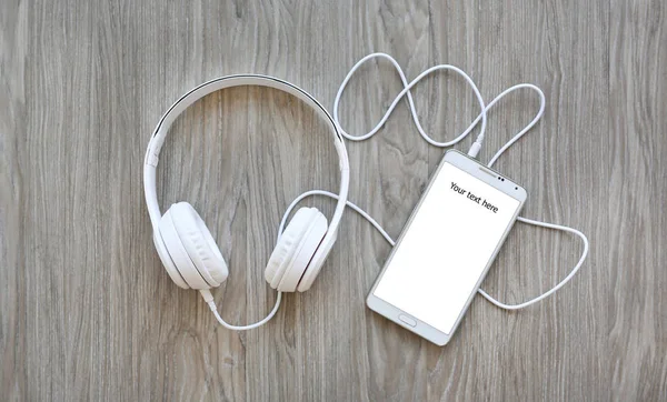 Headphones and smartphone with word "Your text here" on white screen against wooden background — Stock Photo, Image