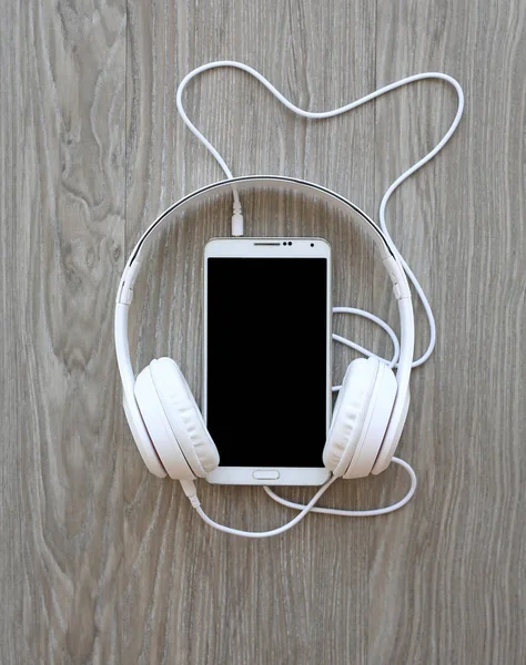 Auriculares y smartphone sobre fondo de madera — Foto de Stock