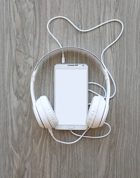 耳机和木制背景上的白色屏幕智能手机 — 图库照片