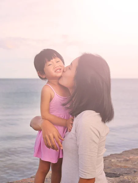Mutlu aile, anne ve çocuk kız akşam deniz arka plan üzerinde gülümseyen doğal duygu ile öpüşme — Stok fotoğraf