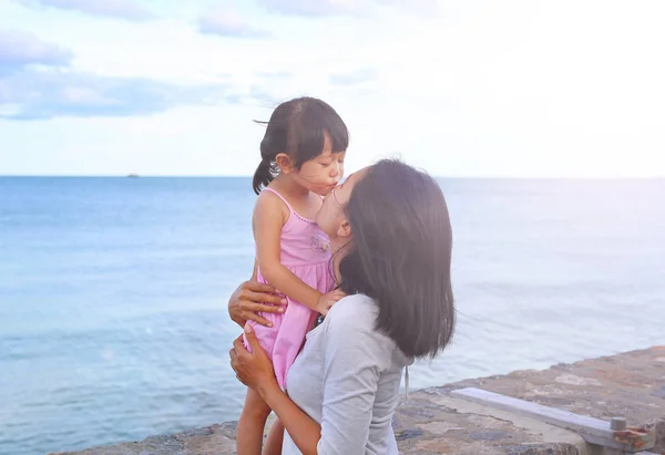 Happy family, mother and kid girl kissing with natural emotion smiling on sea background in the evening