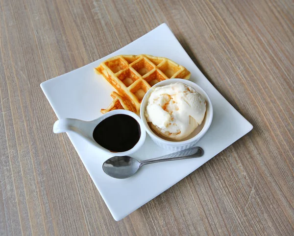 Waffles served with ice cream and chocolate in white plate against wood table — Stock Photo, Image