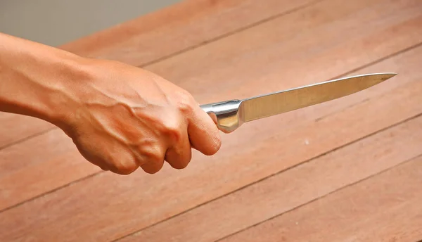 Ein Messer, das mit den Händen gegen Bretterholz gehalten wird — Stockfoto