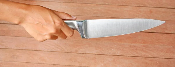 Uma faca sendo segurada por mãos contra a madeira da prancha — Fotografia de Stock