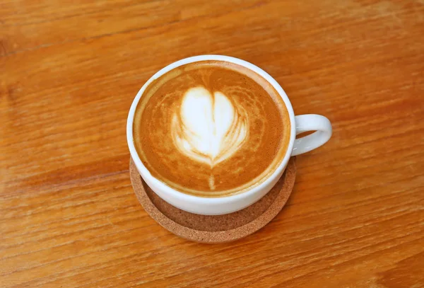 Kalp desenli ahşap zemin, latte sanat üzerine beyaz bir fincan kahve — Stok fotoğraf