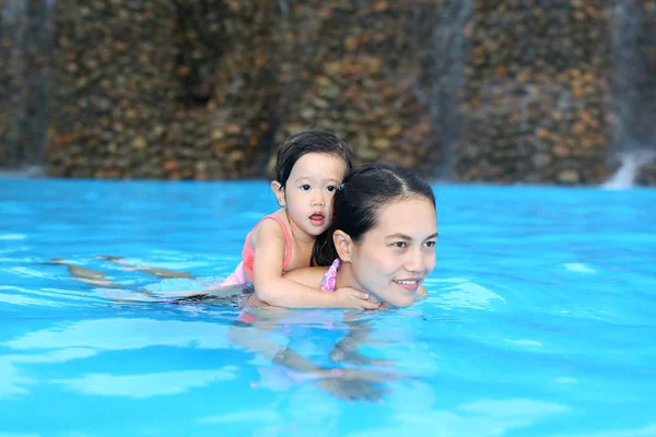 Pretty little girl with her mother playing in swimming pool outdoors — Stock Photo, Image