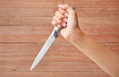 Hand holding a knife ready to strike down against plank wood clipart