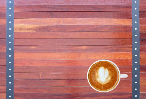 Vista superior de um café com padrão de coração em uma xícara branca em fundo de madeira, arte latte — Fotografia de Stock