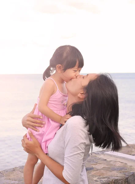 Happy family, mother and kid girl kissing with natural emotion smiling on sea background in the evening — Stock Photo, Image
