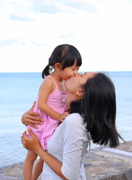 Happy family, mother and kid girl kissing with natural emotion smiling on sea background