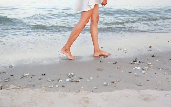Ung kvinna i vit klänning promenerar ensam på stranden — Stockfoto