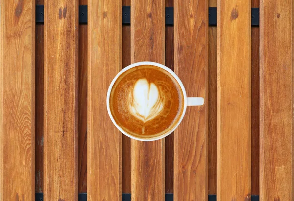 Kalp desenli beyaz bir fincan kahve üstten görünüm ahşap tahta arka plan, latte sanat üzerinde — Stok fotoğraf