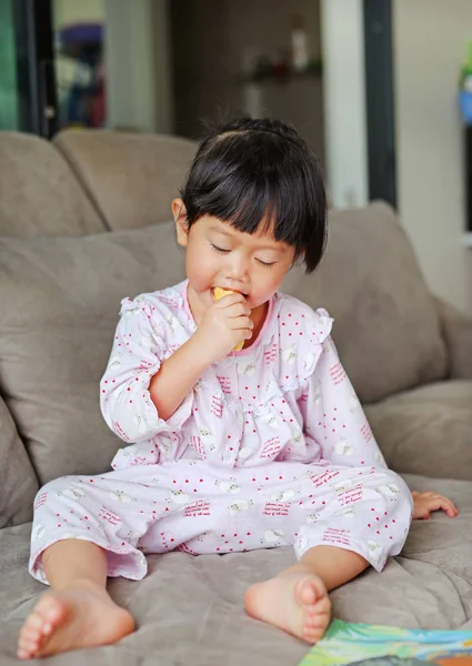 Hermosa niña comiendo plátano en pijama en sofá cama — Foto de Stock
