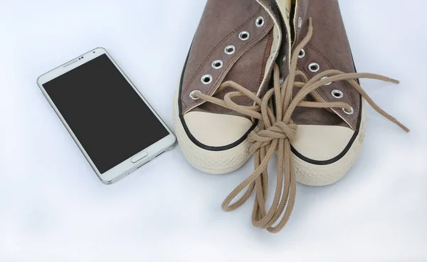 Пара новых кроссовок со смартфоном на белом фоне — стоковое фото