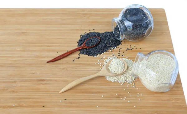 Weißer Sesam und schwarzer Sesam in Flasche und Kochlöffel auf Bambusholzbrett — Stockfoto