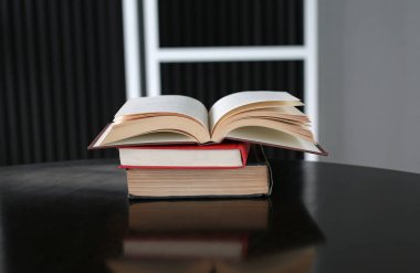 Açık kitap ve ahşap masa üzerinde ciltli kitap yığını.