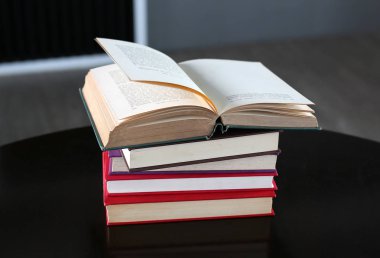 Açık kitap ve ahşap masa üzerinde ciltli kitap yığını.
