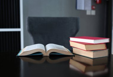 Açık kitap ve ahşap masa üzerinde ciltli kitap yığını.