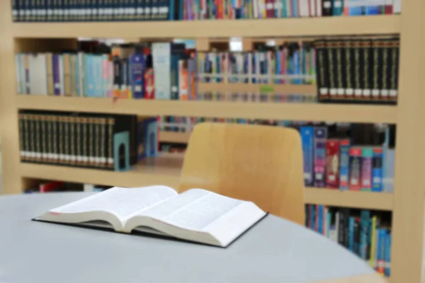 Blurred library with open book on table desk and bookshelf, abstract blur defocused background