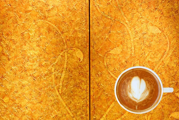 Bovenaanzicht van een kopje koffie met hart patroon in een witte beker op goud patroon achtergrond, Latte art koffie — Stockfoto