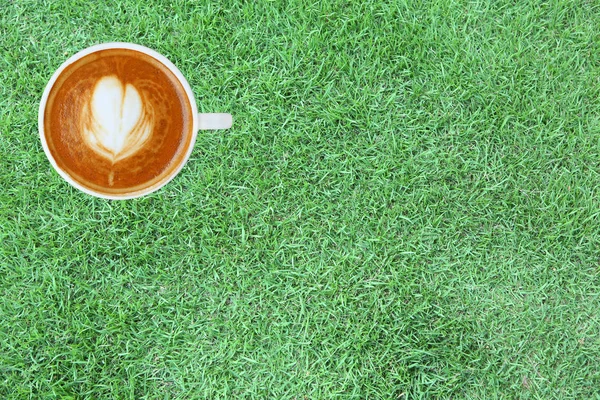 Vista superior de un café con patrón de corazón en una taza blanca sobre fondo de hierba verde, arte latte — Foto de Stock