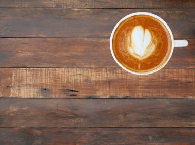 Kalp desenli beyaz bir fincan kahve üstten görünüm ahşap tahta arka plan, latte sanat üzerinde
