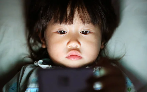 Kid meisje spelen smartphone liggend op een bed bij nacht — Stockfoto