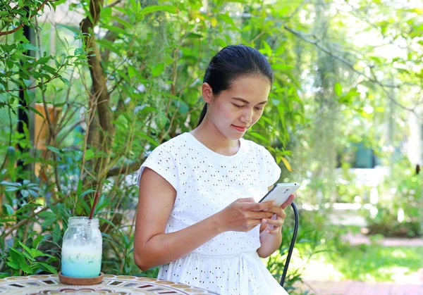 Açık kafede oturan ve akıllı telefon kullanan genç Asyalı kadın — Stok fotoğraf