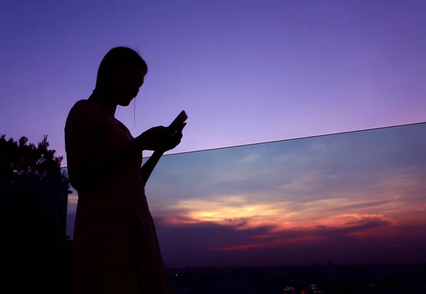 Binanın çatı üzerinde gün batımında smartphone kullanan kadın silüeti — Stok fotoğraf