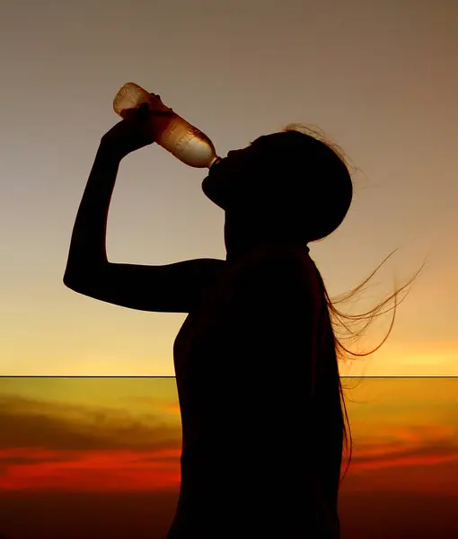 Silhouette de femme Se réhydrater et se rafraîchir au coucher du soleil sur le toit du bâtiment — Photo