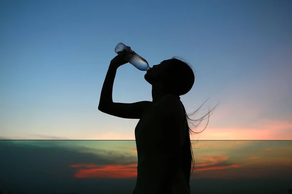 Silhueta de mulher Reidratar e refrescar ao pôr do sol no telhado do edifício — Fotografia de Stock