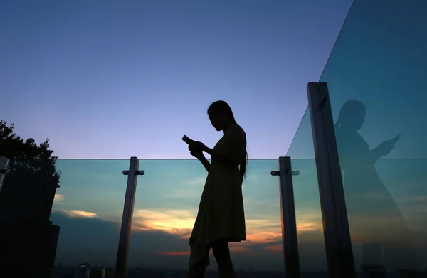 Silhouette of woman using smartphone at sunset on the rooftop of the building — Stock Photo, Image