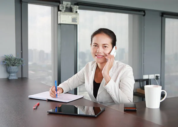 Junge Geschäftsfrau sitzt am Tisch am Arbeitsplatz im Büro und telefoniert — Stockfoto